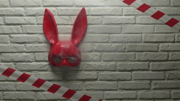 máscara de conejo rojo en una pared de textura de ladrillo blanco y cinta de señal roja y blanca - Imágenes, Vídeo