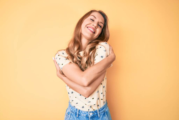 Mulher caucasiana jovem com cabelo loiro vestindo roupas de verão casuais abraçando-se feliz e positivo, sorrindo confiante. auto-amor e auto-cuidado  - Foto, Imagem