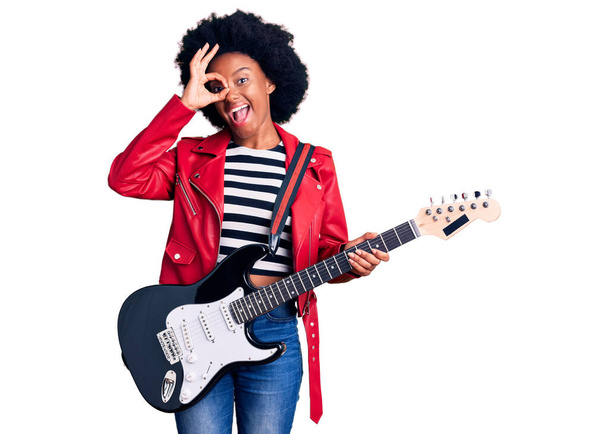 Młoda Afroamerykanka gra na gitarze elektrycznej uśmiechnięta szczęśliwy robi ok znak z ręki na oko patrząc przez palce  - Zdjęcie, obraz