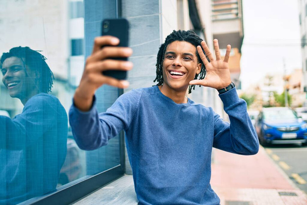 Joven afroamericano haciendo videollamada usando smartphone apoyado en la pared. - Foto, Imagen