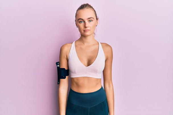Beautiful blonde woman wearing sportswear and arm band relaxed with serious expression on face. simple and natural looking at the camera.  - Valokuva, kuva
