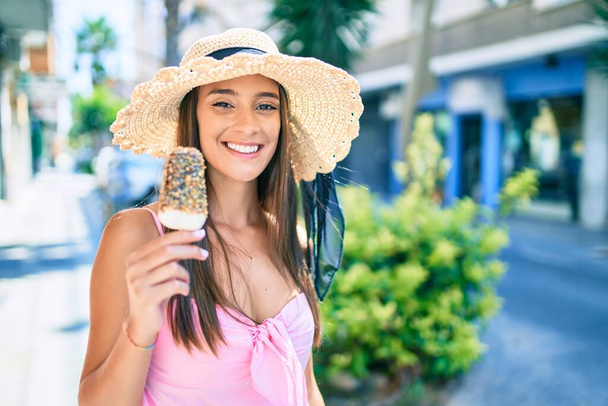 Young hispanic woman on vacation wearing summer style eating ice cream at street of city - Photo, Image