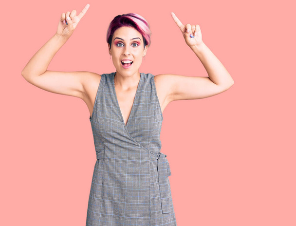 Young beautiful woman with pink hair wearing casual clothes smiling amazed and surprised and pointing up with fingers and raised arms.  - Photo, Image