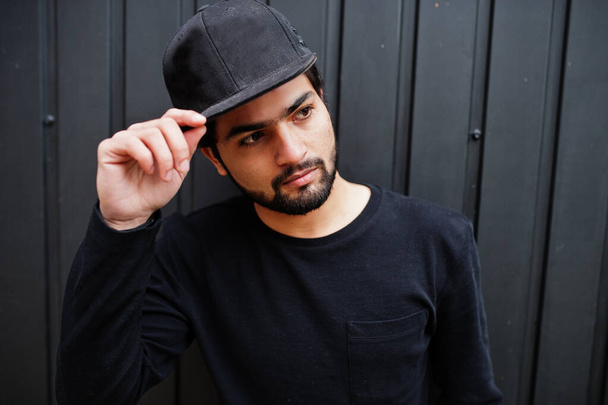 Urban young hipster indian man wear all in black. Cool south asian guy in full cap. - 写真・画像