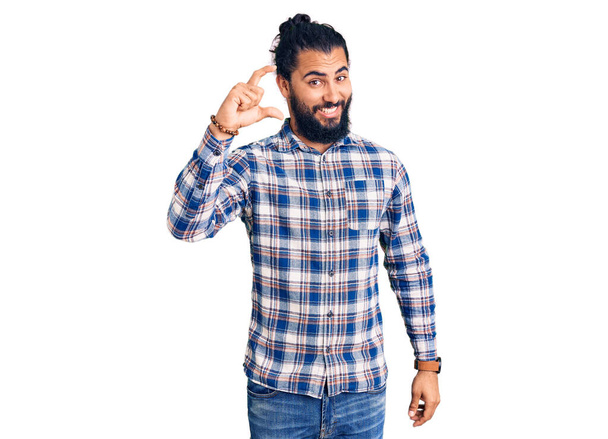 Young arab man wearing casual clothes smiling and confident gesturing with hand doing small size sign with fingers looking and the camera. measure concept.  - Photo, Image
