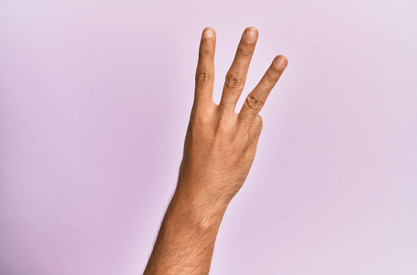 Brazo y mano del joven caucásico sobre fondo rosa aislado contando el número 3 mostrando tres dedos  - Foto, Imagen