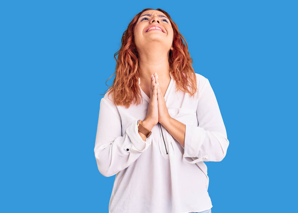Mujer latina joven vestida con ropa casual mendigando y rezando con las manos juntas con expresión de esperanza en la cara muy emotiva y preocupada. mendicidad.  - Foto, Imagen