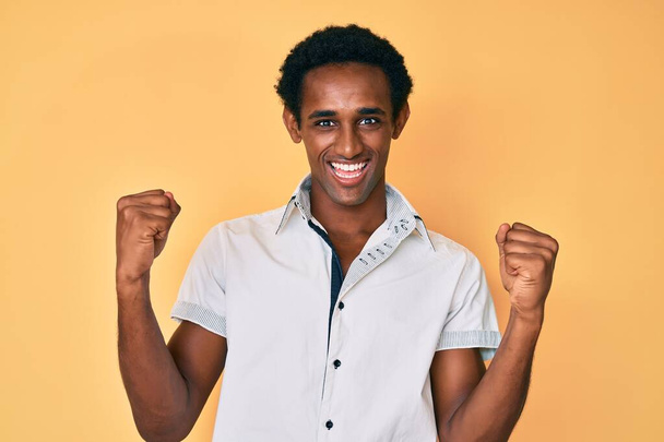 Африканский красивый мужчина в повседневной рубашке кричит гордо, празднует победу и успех очень взволнован с поднятыми руками  - Фото, изображение