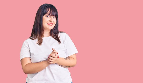 Young plus size woman wearing casual clothes with hands together and crossed fingers smiling relaxed and cheerful. success and optimistic  - Photo, Image