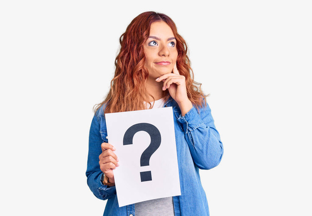 Молодая латинская женщина с вопросительным знаком серьезное лицо думает о вопросе с рукой на подбородке, вдумчиво о запутанной идее  - Фото, изображение