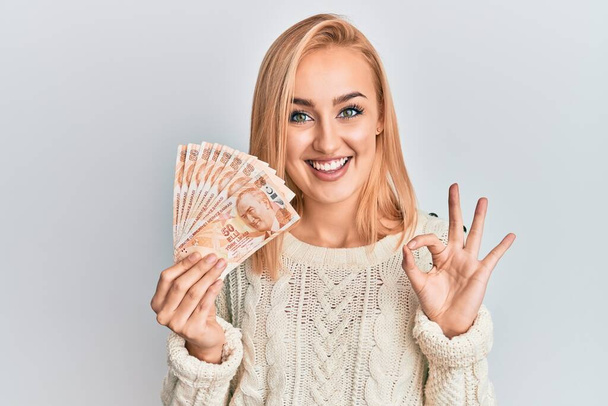 Mooie Kaukasische vrouw met 50 Russische roebel bankbiljetten doen ok teken met de vingers, glimlachend vriendelijk gebaar uitstekend symbool  - Foto, afbeelding