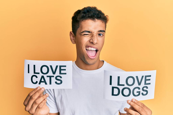 Fiatal jóképű afro-amerikai férfi kezében papír én szeretem macskák és imádom kutyák kifejezés kacsintás nézi a kamera szexi kifejezés, vidám és boldog arc.  - Fotó, kép