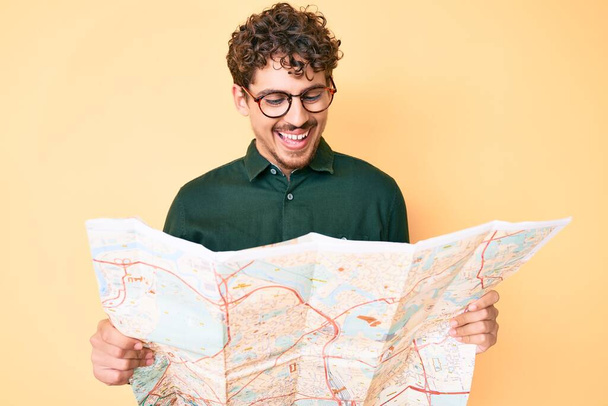 Joven hombre caucásico con el pelo rizado sosteniendo mapa de la ciudad sonriendo y riendo en voz alta porque divertido chiste loco.  - Foto, Imagen