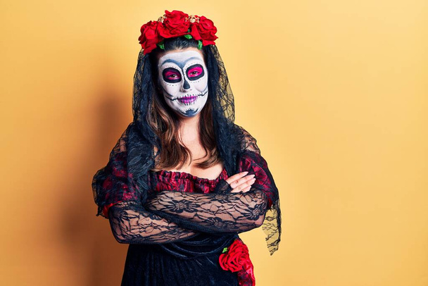 Young woman wearing day of the dead costume over yellow happy face smiling with crossed arms looking at the camera. positive person.  - Photo, image