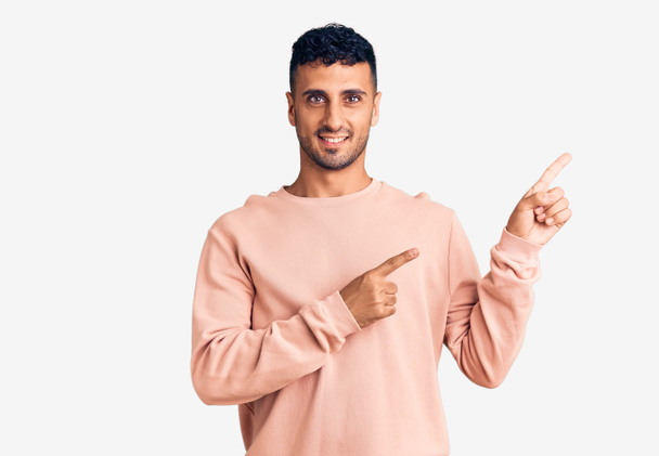Young hispanic man wearing casual clothes smiling and looking at the camera pointing with two hands and fingers to the side.  - Photo, Image