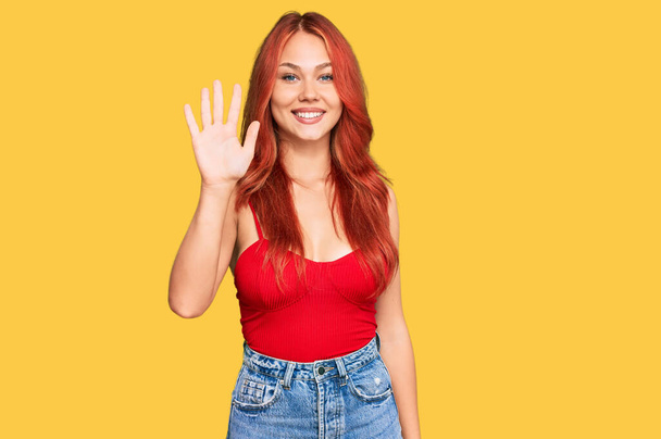 Молодая рыжая женщина в повседневной одежде показывает и указывает пальцами номер пять, улыбаясь уверенно и счастливо.  - Фото, изображение