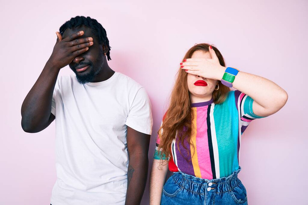 Interracial couple wearing casual clothes covering eyes with hand, looking serious and sad. sightless, hiding and rejection concept  - Photo, Image