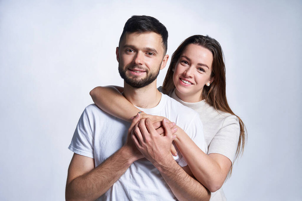 Smiling young couple hugging, studio portrait over light background - Foto, afbeelding