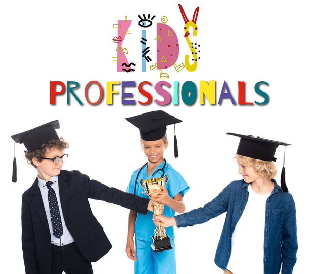 chłopcy i dziewczyna w czapki ukończenia szkoły ubrani w kostiumy różnych zawodów posiadających złote trofeum w pobliżu dzieci profesjonalistów literując na białym  - Zdjęcie, obraz
