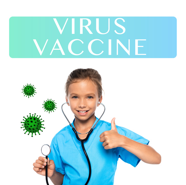 child in costume of doctor holding stethoscope while showing thumb up near virus vaccine lettering on white  - Valokuva, kuva