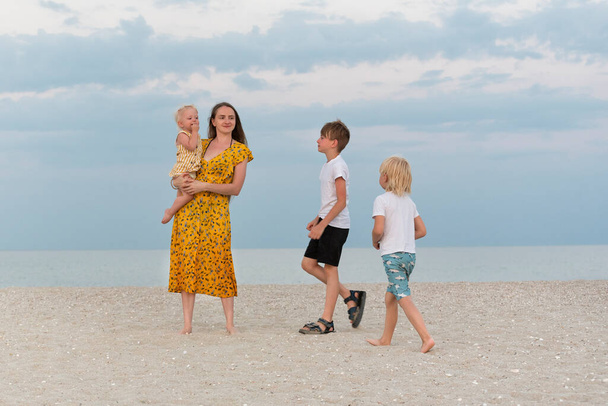 Családi életmód. Anya és három gyermek sétál a homokos tengerparton a tengeri háttér. - Fotó, kép