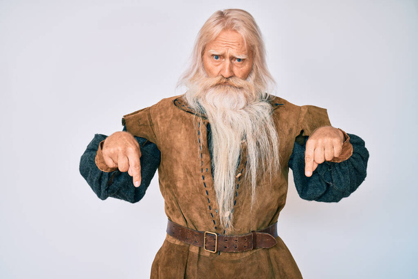 Viejo hombre mayor con pelo gris y barba larga vikingo traje tradicional apuntando hacia abajo buscando triste y molesto, indicando la dirección con los dedos, infeliz y deprimido.  - Foto, imagen