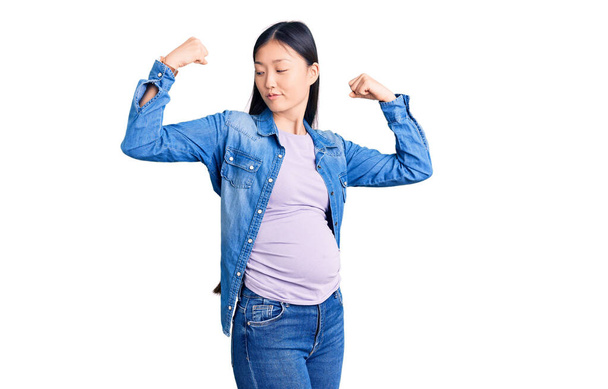 若い美しい中国の女性妊娠中の赤ちゃん腕の筋肉を示すことを期待誇りに思って笑顔。フィットネスのコンセプト.  - 写真・画像