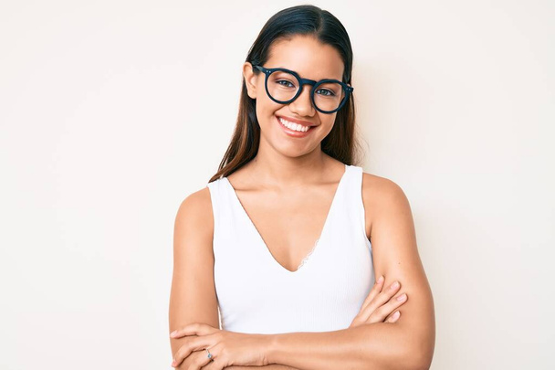 Fiatal, gyönyörű latin lány alkalmi ruhát és szemüveget visel boldog arc mosolyogva keresztbe tett karokkal nézi a kamerát. pozitív személy.  - Fotó, kép