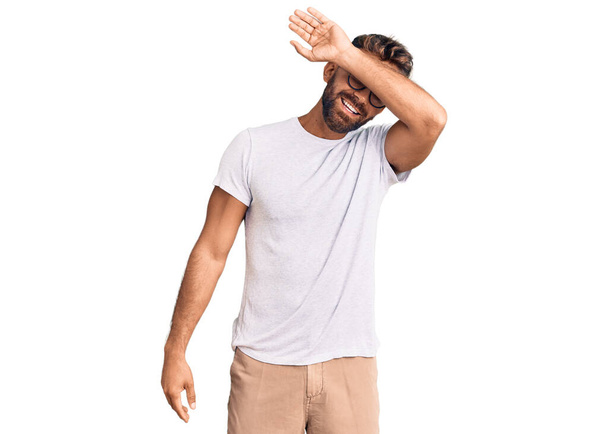 Young hispanic man wearing casual clothes and glasses covering eyes with arm smiling cheerful and funny. blind concept.  - Foto, Bild