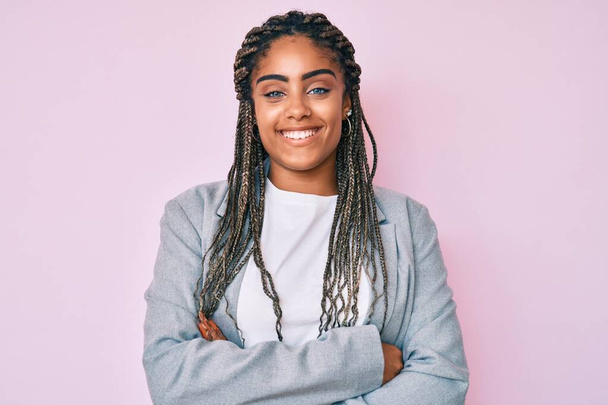 Młoda Afroamerykanka z warkoczami w biznesowej kurtce uśmiechnięta z skrzyżowanymi ramionami patrząca w kamerę. osoba pozytywna.  - Zdjęcie, obraz
