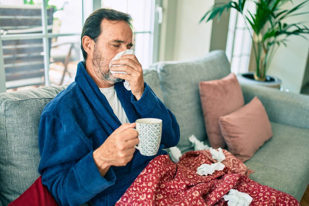 Mann mittleren Alters krank mit Erkältung und Fieber zu Hause, krank mit Grippe auf dem Sofa sitzend - Foto, Bild