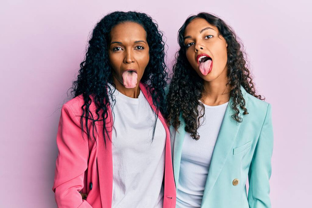 African american mother and daughter wearing business style sticking tongue out happy with funny expression. emotion concept.  - Foto, Bild