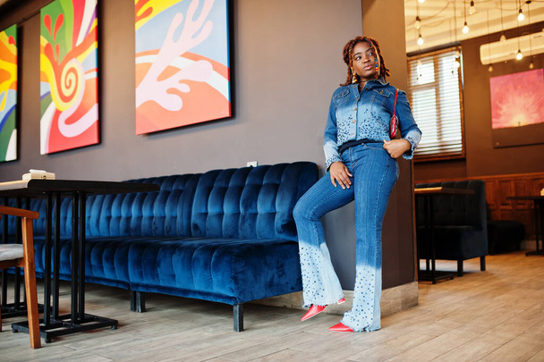 Lovely african american woman with dreadlocks in blue stylish jeans jacket at cafe. Beautiful cool fashionable black young girl indoor. - Foto, Imagen