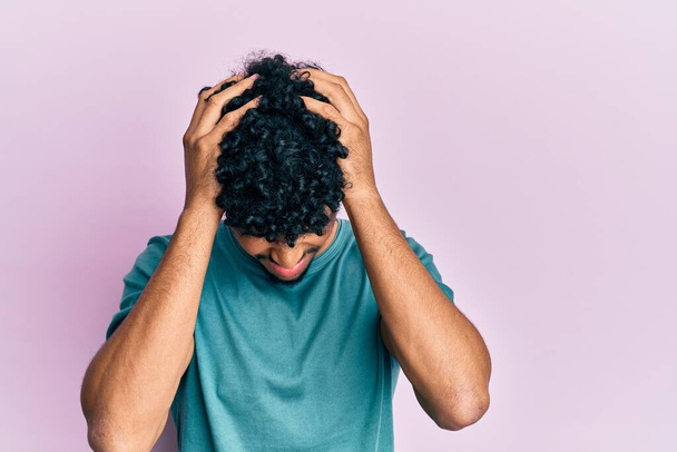 Mladý arabsky pohledný muž v neformálním oblečení trpí bolestí hlavy zoufalý a vystresovaný, protože bolest a migréna. Ruce za hlavu.  - Fotografie, Obrázek