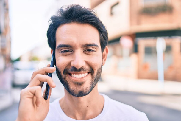 Giovane uomo ispanico sorridente felice parlando sullo smartphone in città. - Foto, immagini