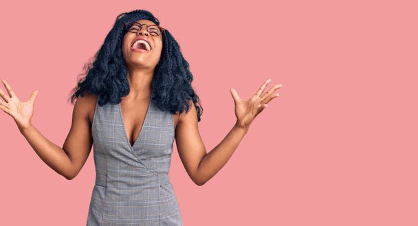 Krásná africká americká žena v obchodních šatech a brýlích slaví šílený a šílený úspěch s rukama zvednutýma a zavřenýma očima křičí vzrušeně. koncept vítěze  - Fotografie, Obrázek