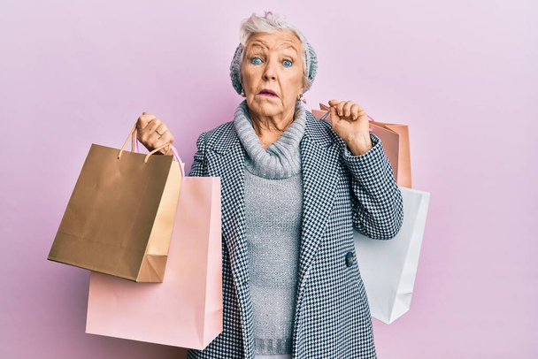 Idősebb ősz hajú nő, bevásárlószatyrokkal a kezében, tanácstalan és zavaros arckifejezéssel. kétség.  - Fotó, kép