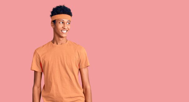 Fiatal afro-amerikai férfi, aki sportruházatot visel, arcán mosollyal, természetes kifejezéssel néz félre. nevetés magabiztos.  - Fotó, kép