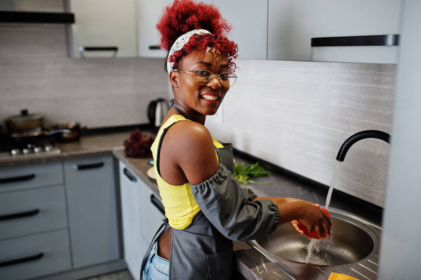 Mulher afro-americana preparando comida saudável em casa cozinha. Ela lava produtos em lavatório. - Foto, Imagem
