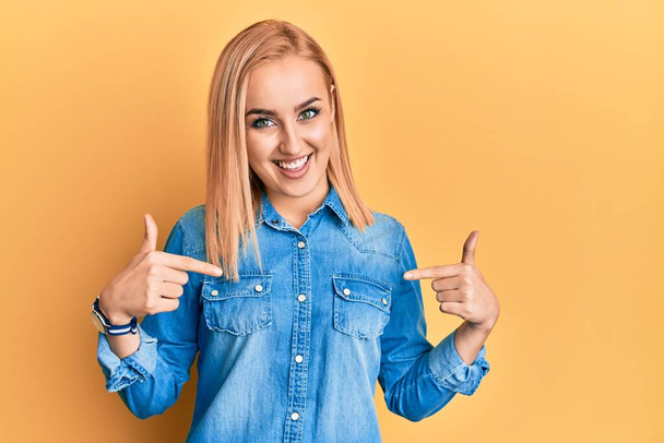 Schöne kaukasische Frau in lässiger Jeansjacke sieht selbstbewusst aus mit einem Lächeln im Gesicht und zeigt stolz und glücklich mit den Fingern.  - Foto, Bild