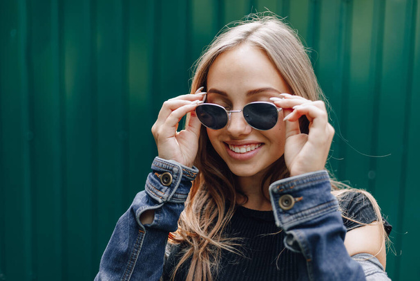 junges hübsches attraktives Mädchen in Jeanskleidung in Brille auf einfachem dunkelgrünem Hintergrund mit leerem Platz für Text. - Foto, Bild