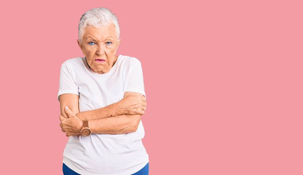 Senior beautiful woman with blue eyes and grey hair wearing casual white tshirt shaking and freezing for winter cold with sad and shock expression on face  - 写真・画像