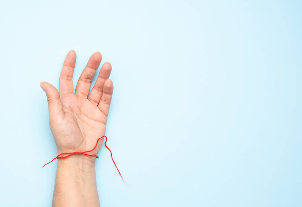 red woolen thread on the wrist of a female hand, blue background, copy space - Фото, изображение
