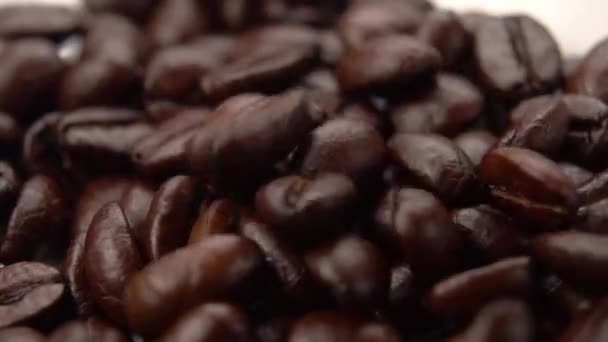 Roasted coffee grains close up are pouring into a heap. Macro shot. Slow motion - Materiał filmowy, wideo