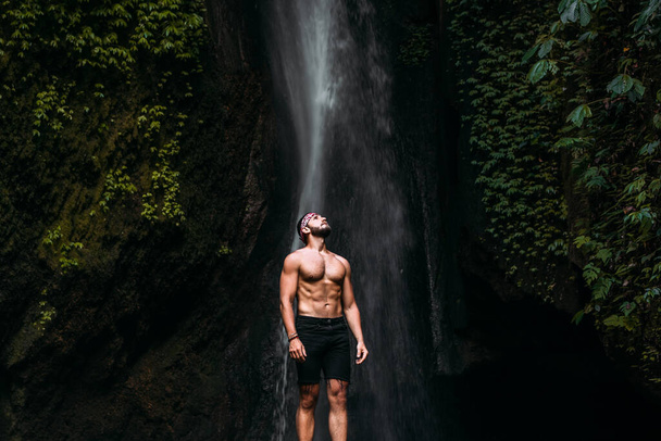 A man of athletic build at the waterfall. A man travels the world. Man at the waterfall. Travel to Bali Indonesia. Lone traveler. Copy space - Foto, immagini