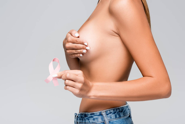 Cropped view of woman touching breast and holding pink ribbon of breast cancer awareness isolated on grey  - Photo, image