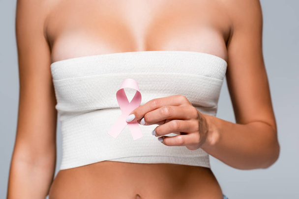 Cropped view of woman with elastic bandage on breast holding sign of breast cancer awareness isolated on grey  - Фото, изображение
