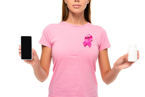 Περικοπή άποψη της γυναίκας με κορδέλα του καρκίνου του μαστού ευαισθητοποίηση κρατώντας smartphone και χάπια που απομονώνονται σε λευκό - Φωτογραφία, εικόνα