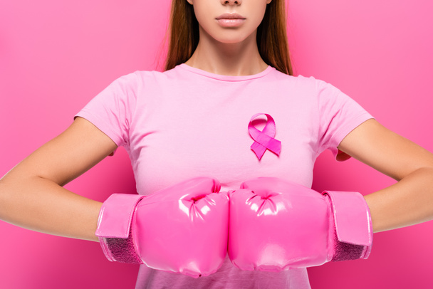 Vista ritagliata di giovane donna in guanti da boxe rosa e nastro di consapevolezza del cancro al seno su sfondo rosa  - Foto, immagini