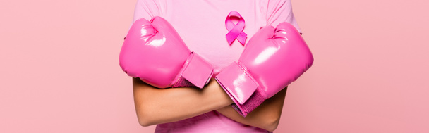 Καλλιεργημένη άποψη της γυναίκας σε γάντια πυγμαχίας και ροζ σημάδι της ευαισθητοποίησης του καρκίνου του μαστού απομονώνονται σε ροζ, πανό  - Φωτογραφία, εικόνα